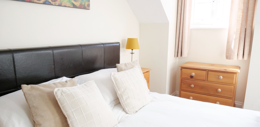side image of bed with a window in the background and a chest of drawers