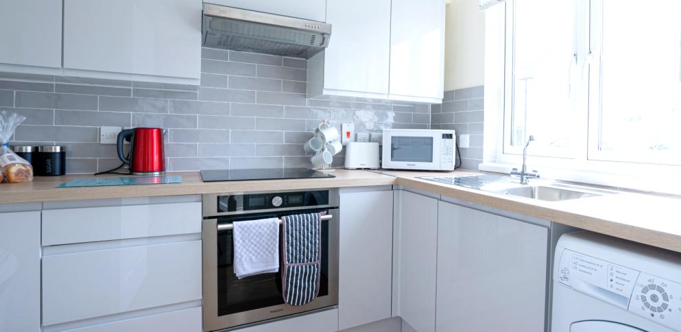 kitchen with glossy grey units and natural wood worktop and red kettle