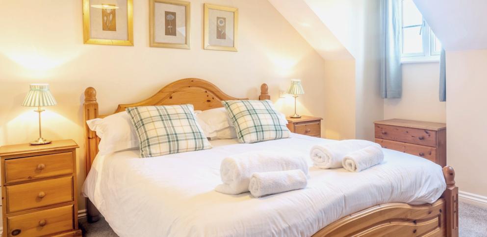 large pine bed with white sheets and green/yellow striped cushions.  Three gold framed pictures above.