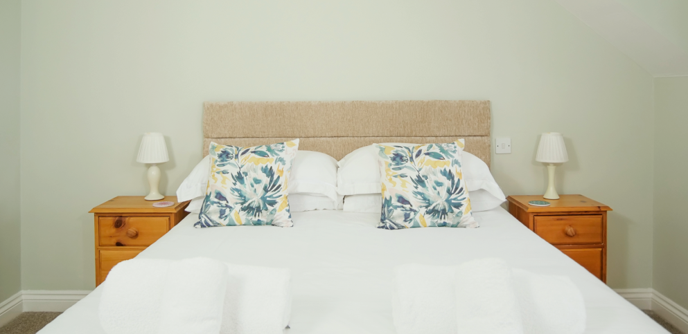 king size bed with cream headboard.  Pale blue walls and blue/yellow cushions