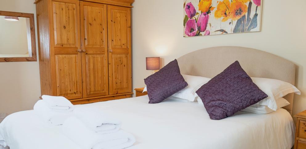 large bed with white duvet cover and cream curved headboard. Large pine wardrobe to rear