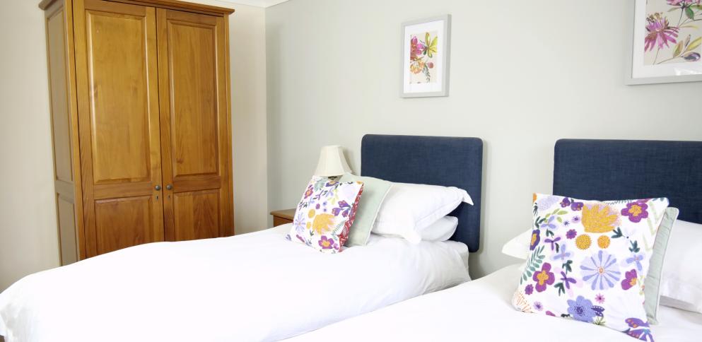two single beds with blue headboards and brghtly patterned cushions. Oak wardrobe in background