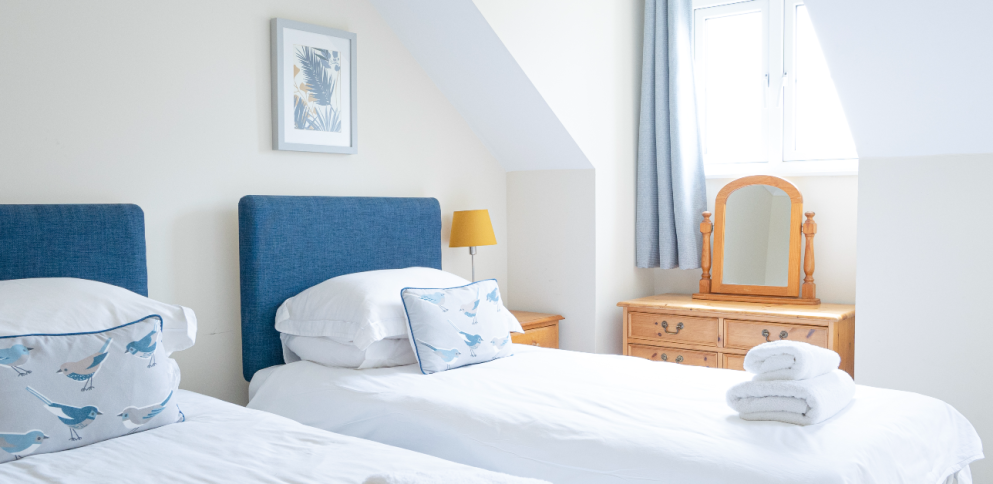 single beds with blue headboards, with a pine mirror sitting on top of a chest of drawers